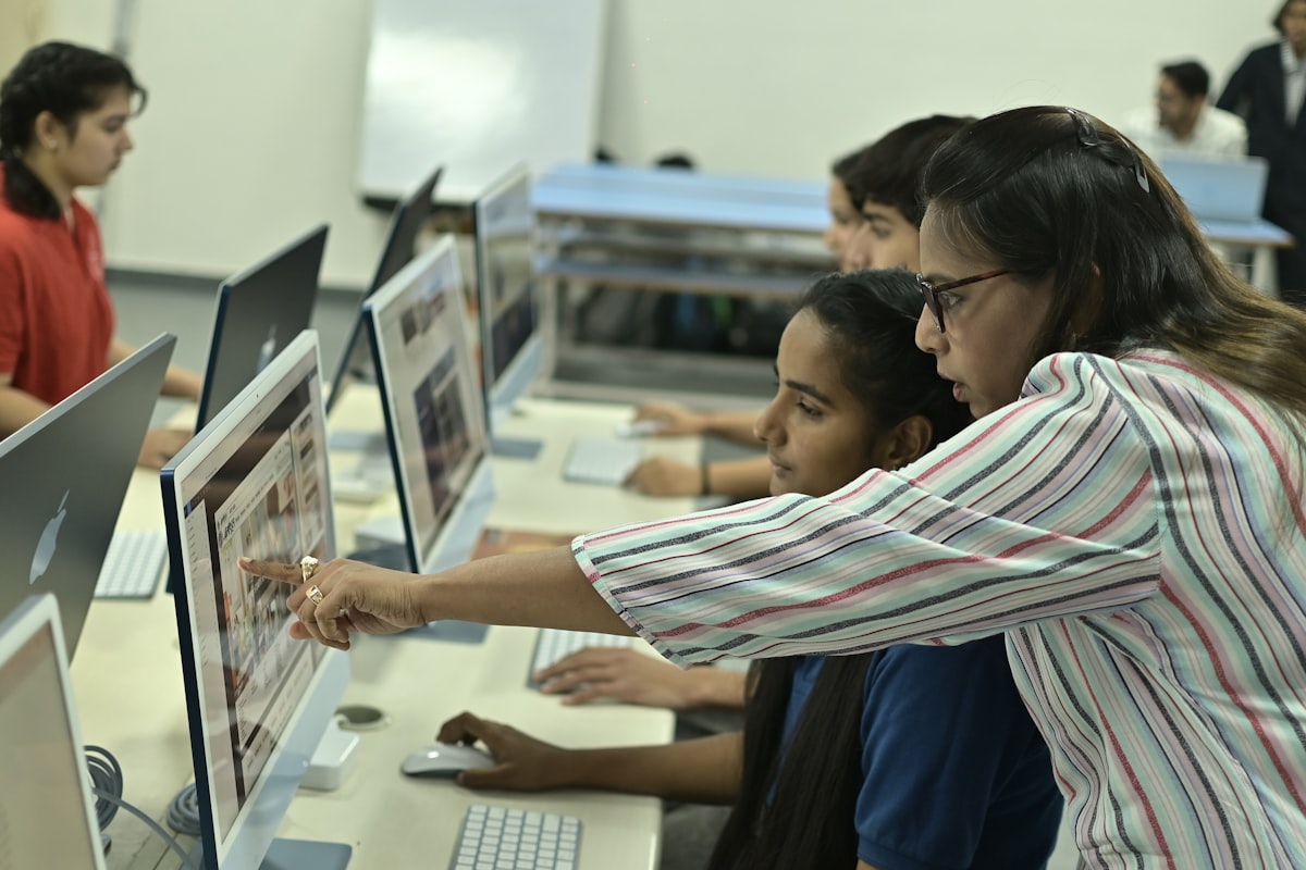 A teacher guiding students at computers in a classroom