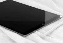 A tablet lying screen-down on a bed with a stylus resting beside it