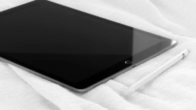 A tablet lying screen-down on a bed with a stylus resting beside it