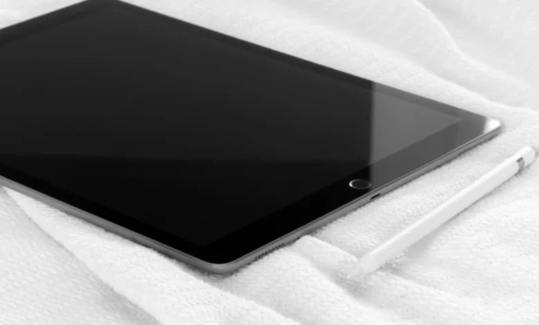 A tablet lying screen-down on a bed with a stylus resting beside it