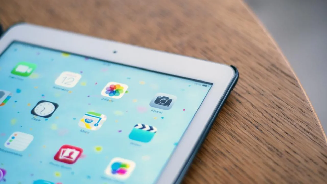A tablet on a wooden table showing a home screen full of app icons