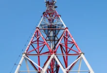 A red and white mobile network tower against a clear blue sky