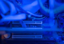 Close-up inside a gaming PC case showing cables, PCIe slots and a CPU cooler fan under blue light