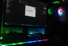 A Windows desktop PC screen mid file-copy next to an RGB-lit gaming tower in a dark room
