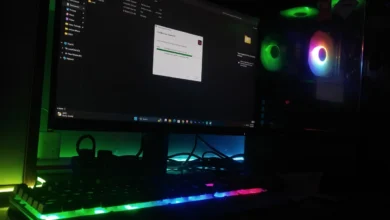 A Windows desktop PC screen mid file-copy next to an RGB-lit gaming tower in a dark room