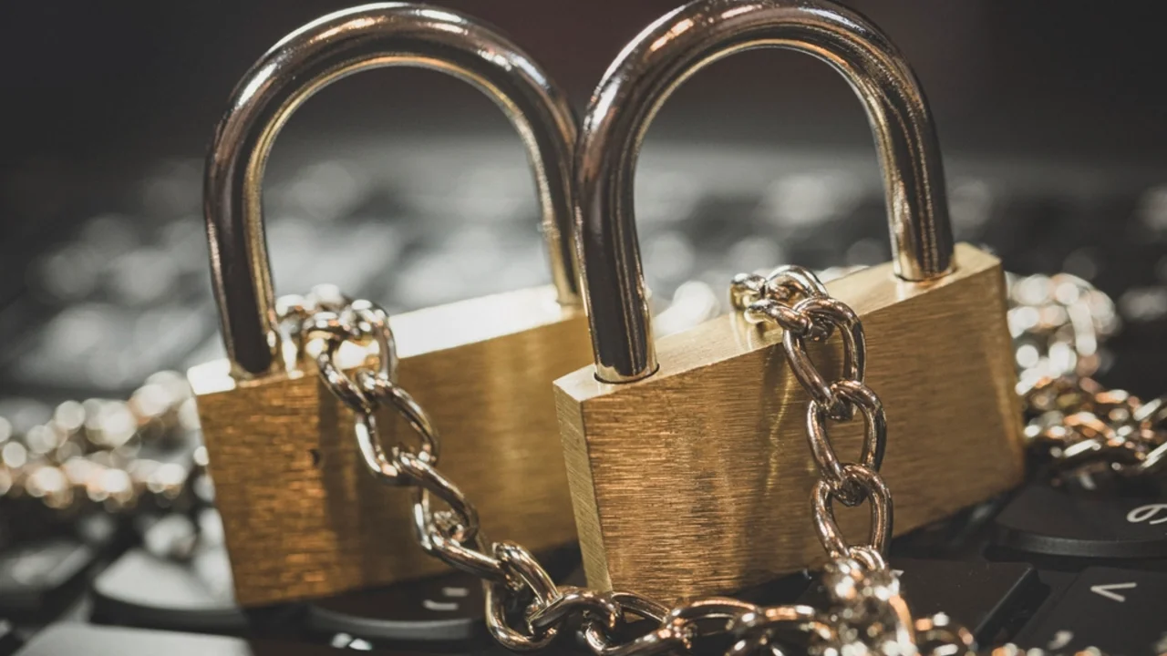 Two brass padlocks wrapped in metal chains resting on a computer keyboard